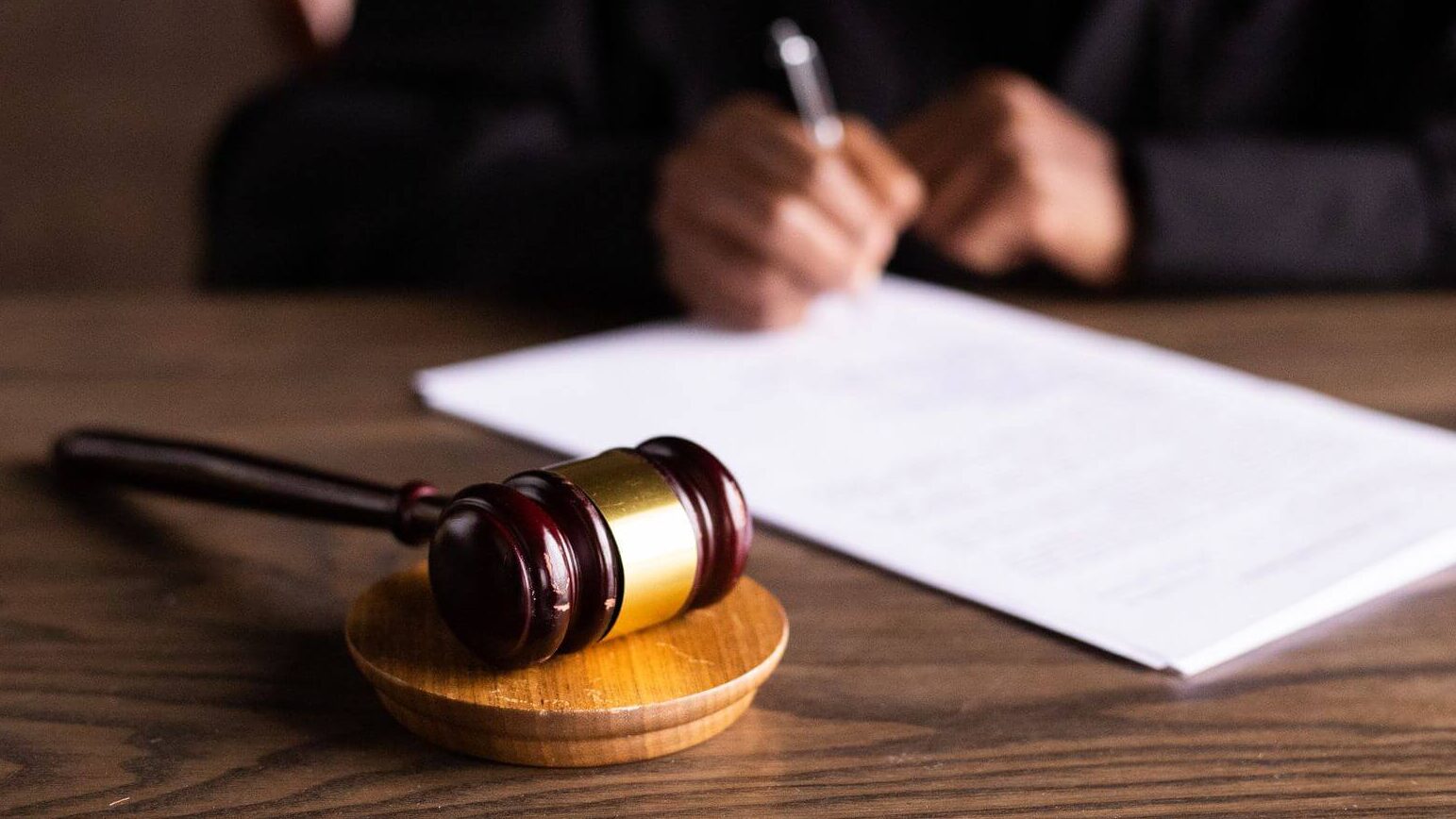 judge signing legal document with gavel on table